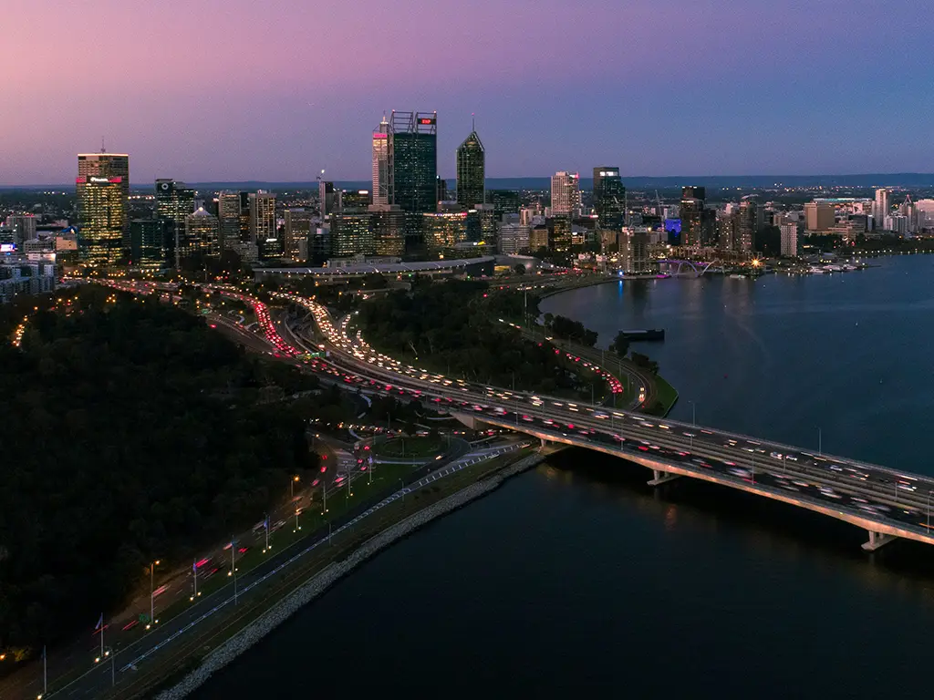 Drone photo of Narrows Bridge underpass with city in background and purple sky at dusk.
