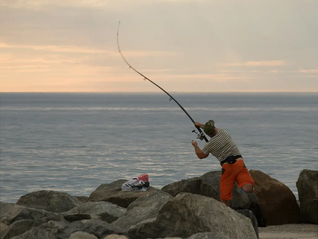 Fisher at North Mole, Fremantle WA casting long beach rod into ocean at dusk.