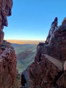 Scramble up Mount Bruce cliff face in Karijini National Park, with female hiker in background on edge of cliff.