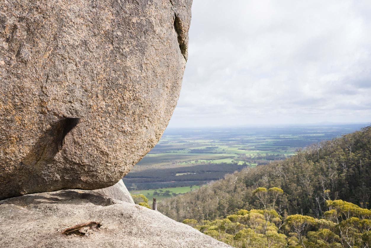 Image of boulder rock, Perth Hills WA, with valley and grey clouds in background.