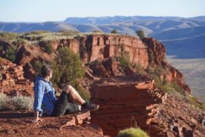 Male hiker in blue collared shirt at peak on Mount Bruce overlooking Karijini National Park