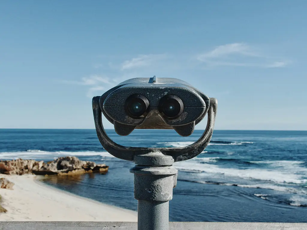 Binoculars facing West End in Rottnest Island with blue sky and glassy ocean in front of fishing beach.
