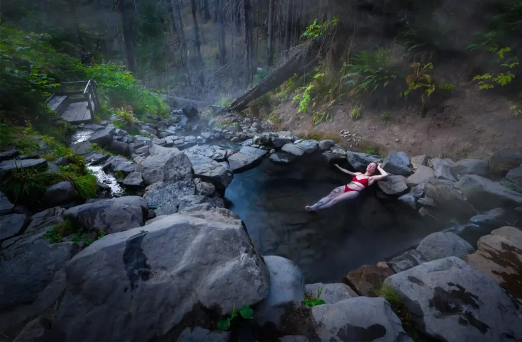 Woman lying in hot spring in Western Australia surrounded by smooth grey rocks and forest