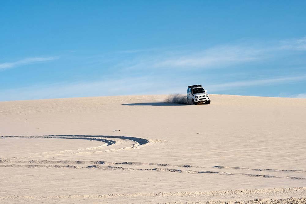 4WD on sand dunes making large turn with blue sky in background