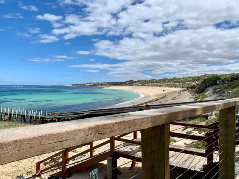 Blue sky and white clouds above Prevelly Beach in Margaret River along the Cape to Cape trail, with Indian Ocean meeting white sandy shores from wooden stairwell lookout.