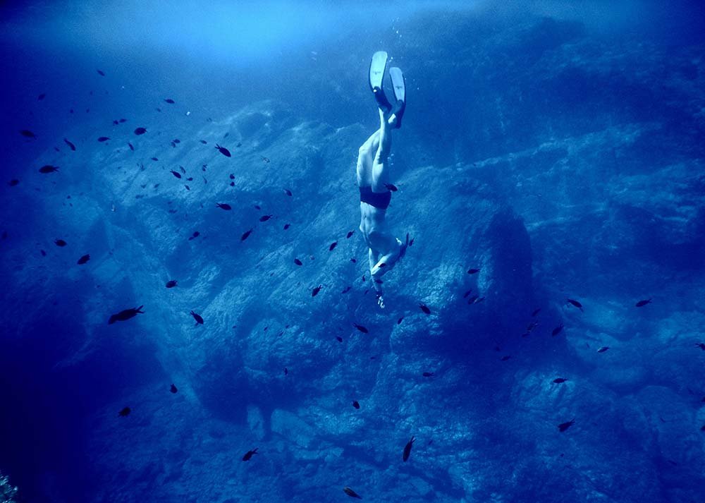 Freediver kicking downward under ocean towards shipwreck