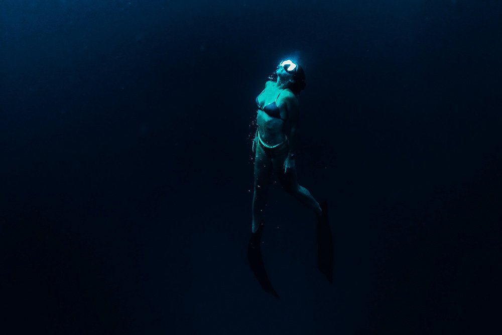 Female freediver in dark ocean submerging after using mammalian dive reflex to submerge herself.
