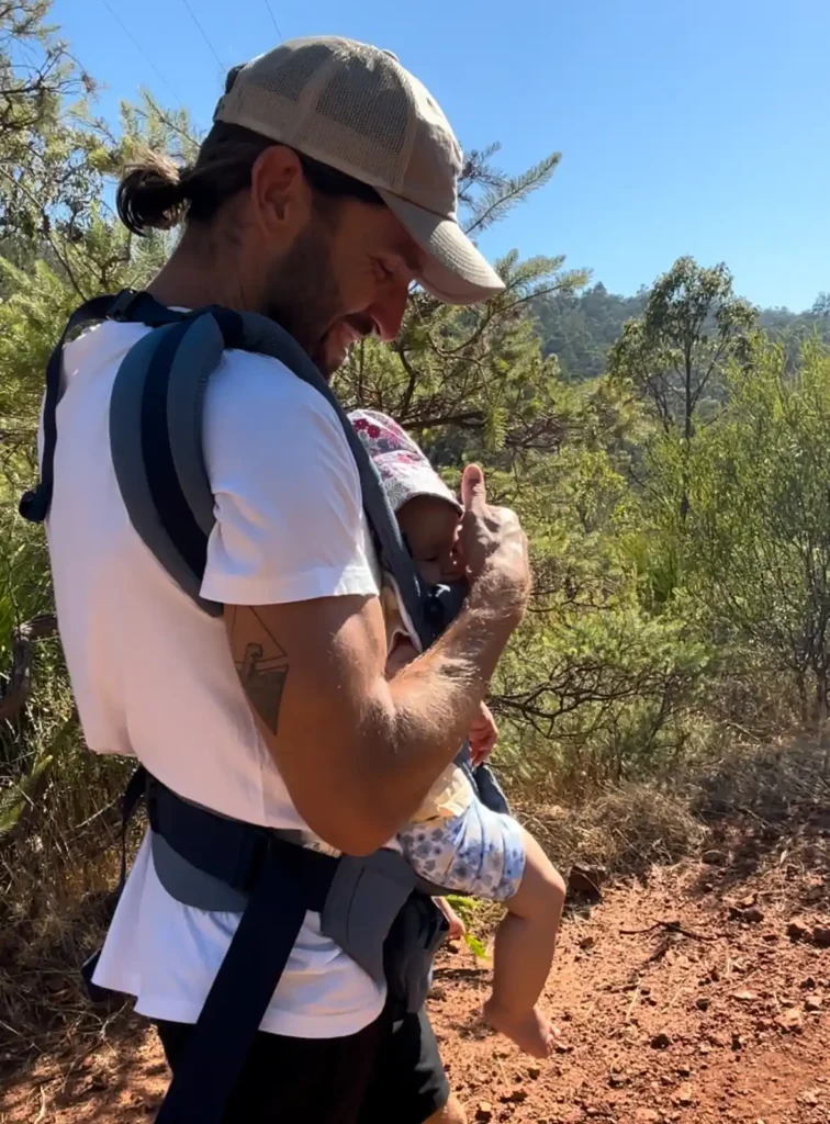 Hiker with baby in carrier on his chest while walking on Perth Hills hiking trail on blue sky day