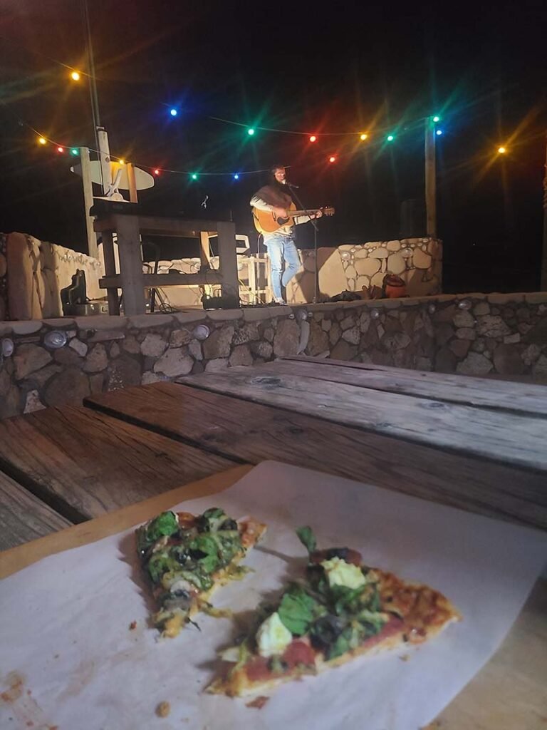 Man singing on stage at Open Mic night in Red Bluff WA, with slice of pizza on table in front of photographer