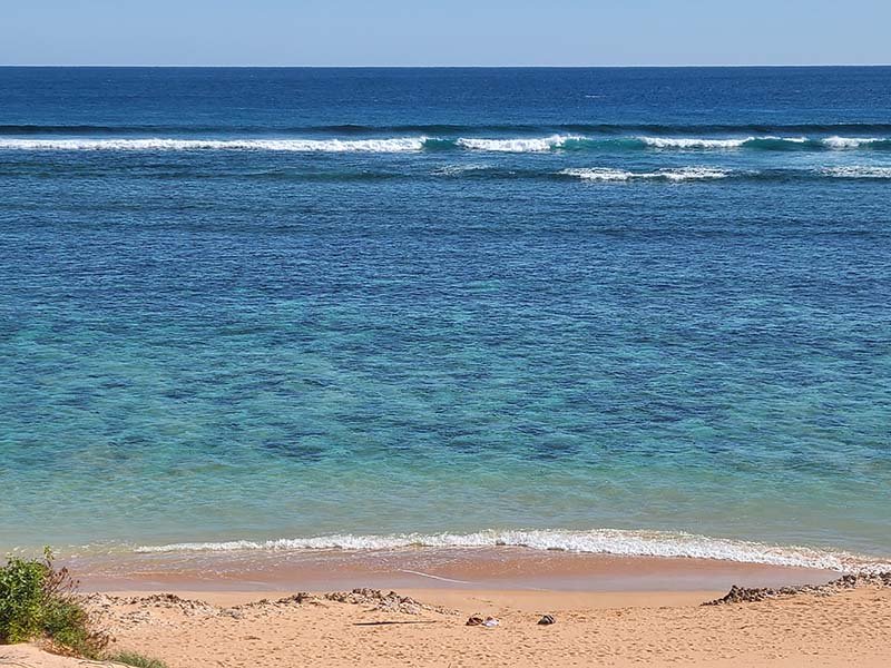 Image of beach at Red Bluff in WA, with turquoise waters meeting white sand with waves breaking near horizon.