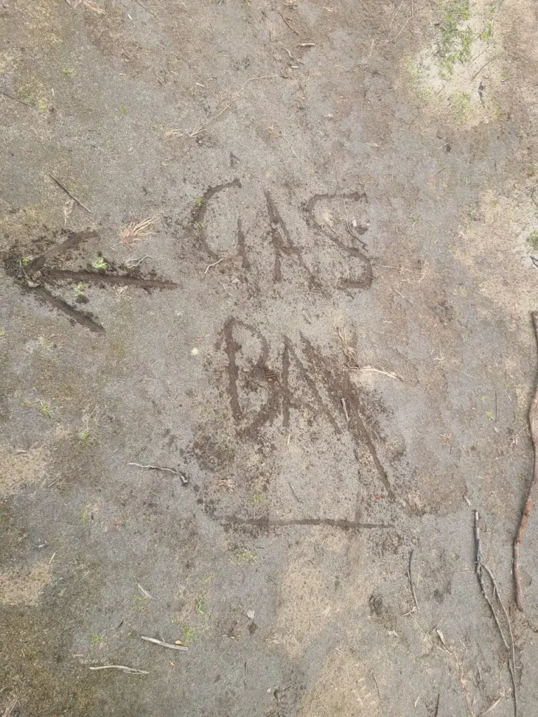 Directions written in sand saying Gas Bay with arrow pointing to running trail car park