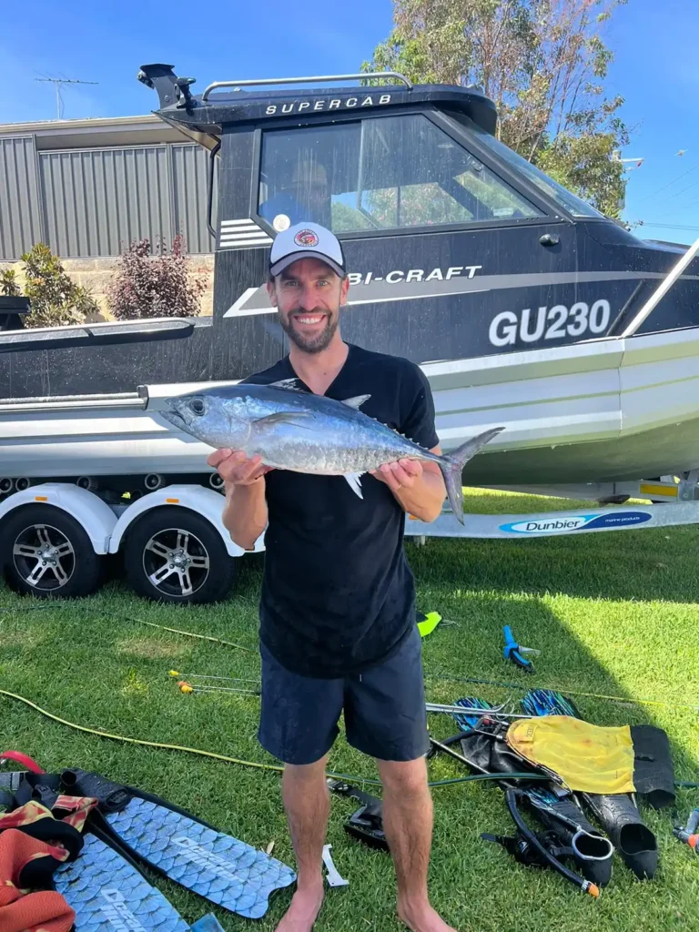 Photo of man holding tuna on grass of Perth property front lawn with fishing boat in the background.