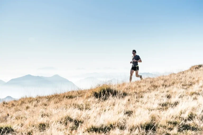 Trail runner wearing short sleeve shirt and trail running shorts on steep gradient in middle of day with mountain silhouette in background