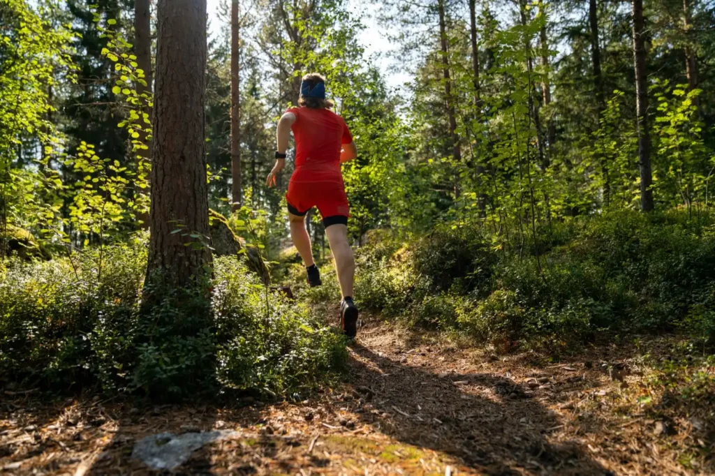 Rear shot of trail runner running through woods wearing bright red outfit