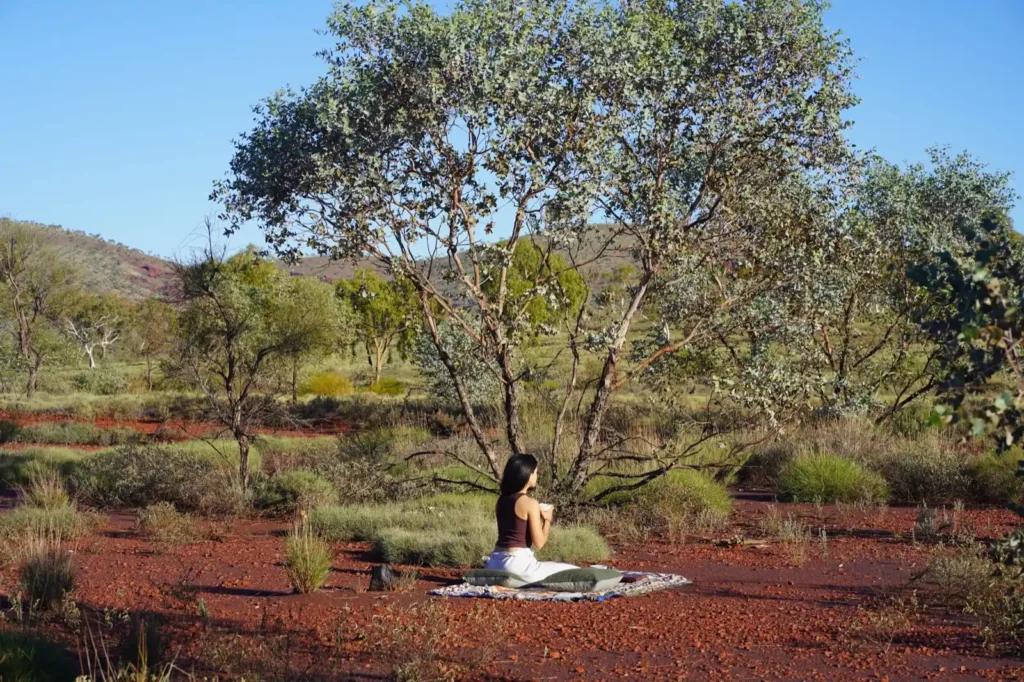 Woman drinking tea alone among the bush and red dirt in Dales campground near Karjini National Park and Mount Bruce
