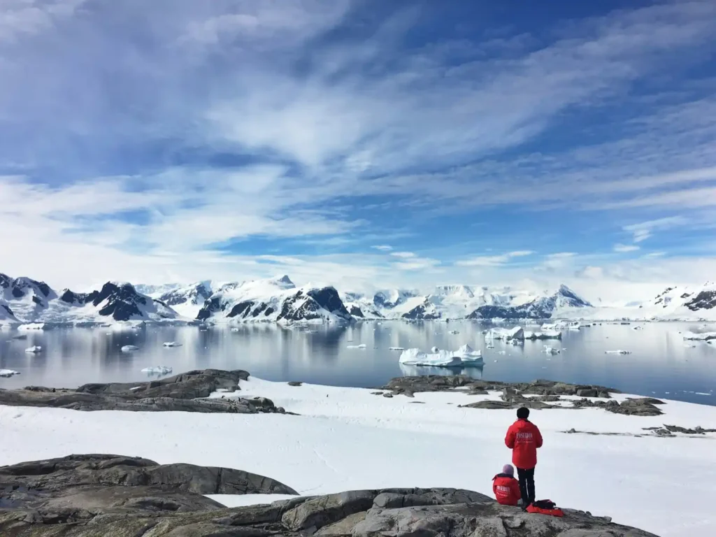 A researcher in red outfit standing on the bank of a sheet of ice in Antarctica under a blue sky