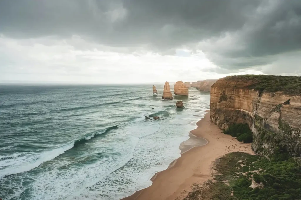Drone shot of The Twelve Apostles in Victoria on a cloudy day, waves rolling into the shoreline. 
