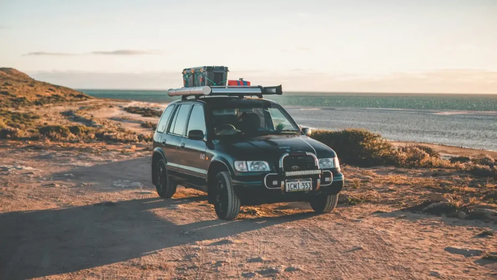 Packed 4WD at a secluded camping spot near Perth, West Australia, with ocean in background and white sky, dirt terrain and hills.