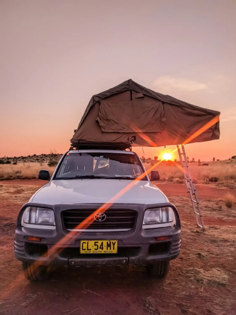 A 4WD in Perth, West Australia with its rooftop tent folded out and the sun setting in the background at a secluded off-grid camping spot.